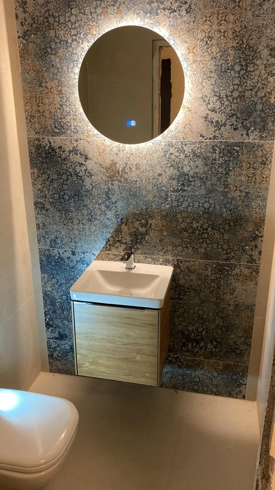 Gäste-WC mit Waschtisch, rundem beleuchtetem Spiegel und gemusterten Wandfliesen