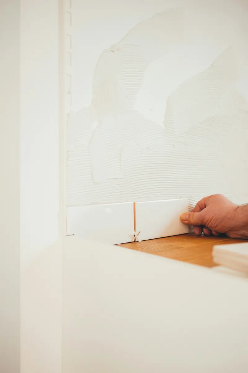 Hand setzt eine weiße Wandfliese ins Kleberbett